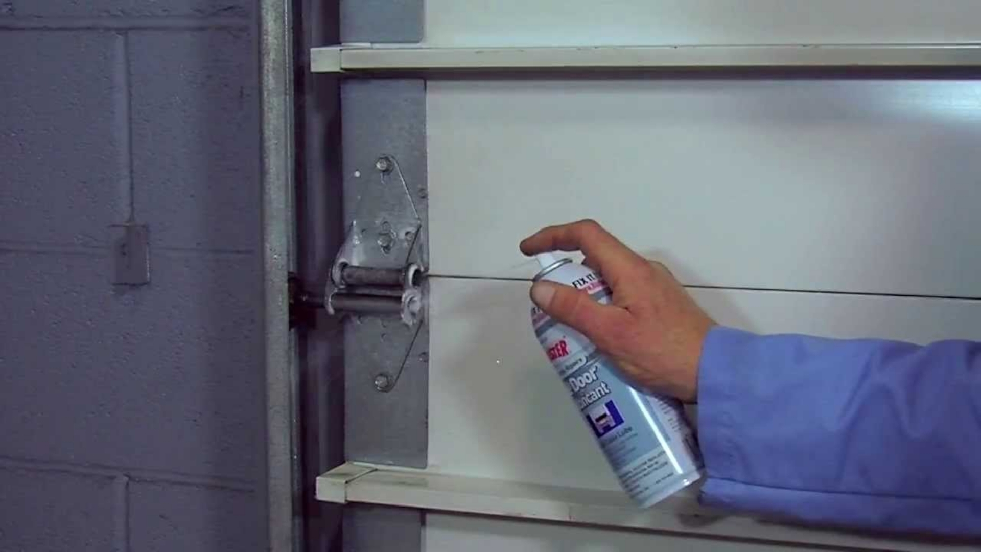 A man spraying a garage door lubricant on the hinges