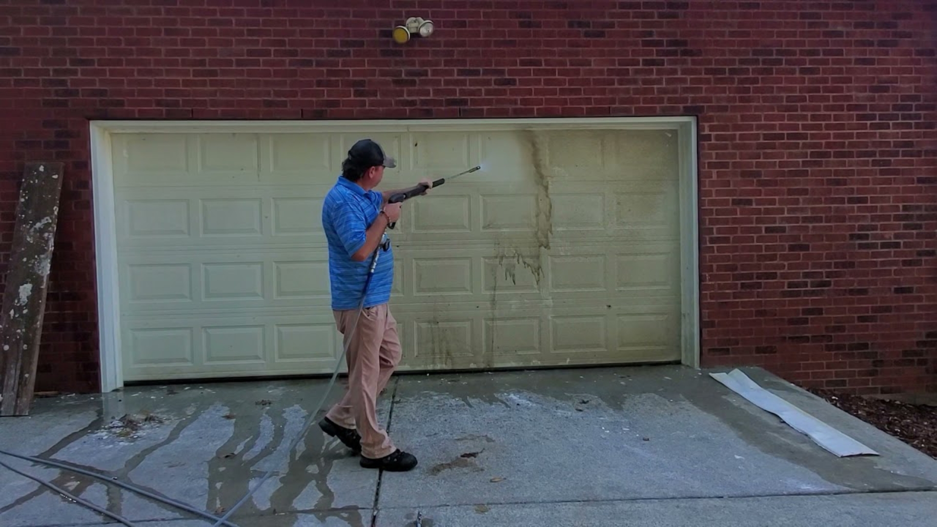 A homeowner cleaning a garage door with a pressure washer to remove dirt and stains before painting