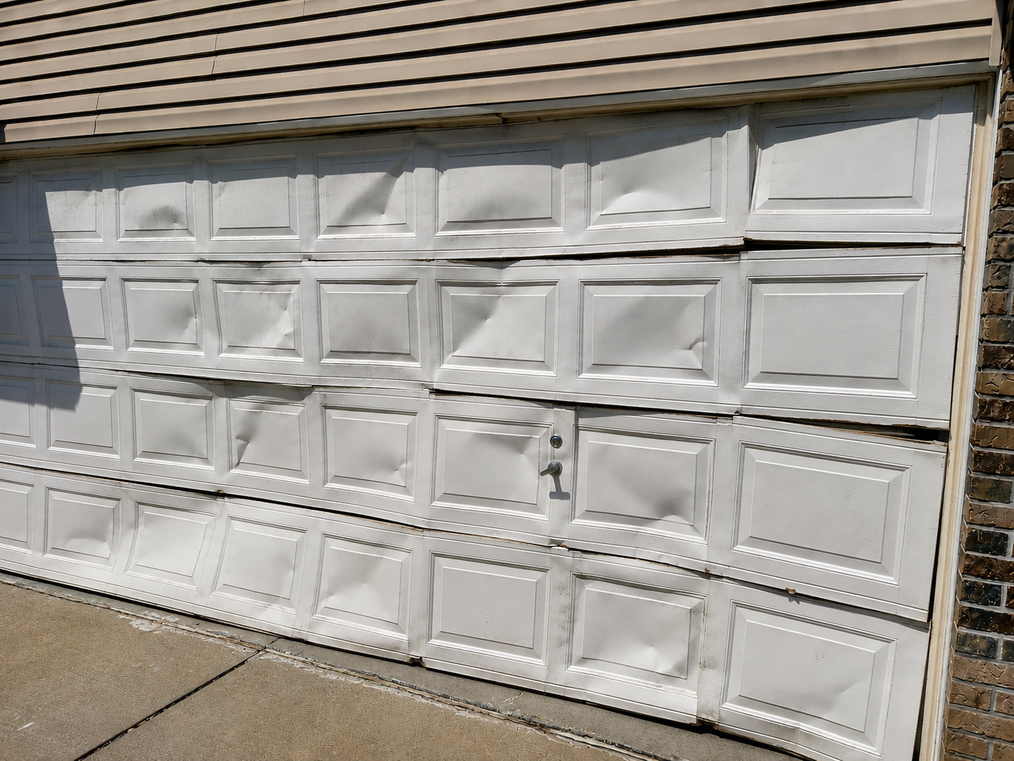 Garage door panel repair showing a sectional garage door with multiple dented, bent, and misaligned panels after impact damage.