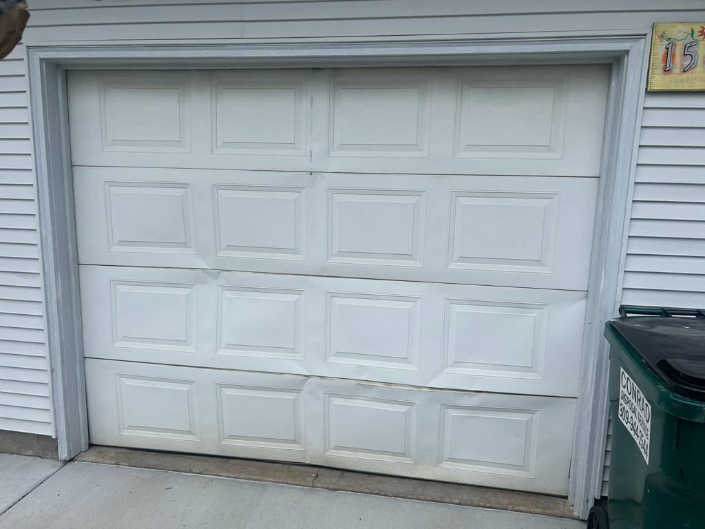 Garage door panel repair showing a residential sectional garage door with multiple dented panels 