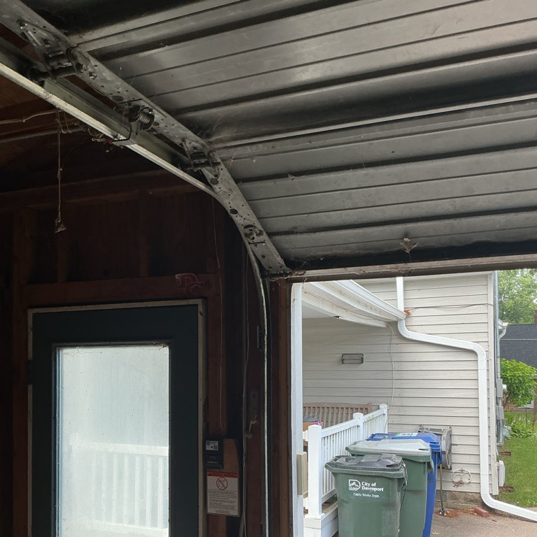 Garage door roller repair showing the curved track, hinges, and roller assembly on an open residential garage door before maintenance.