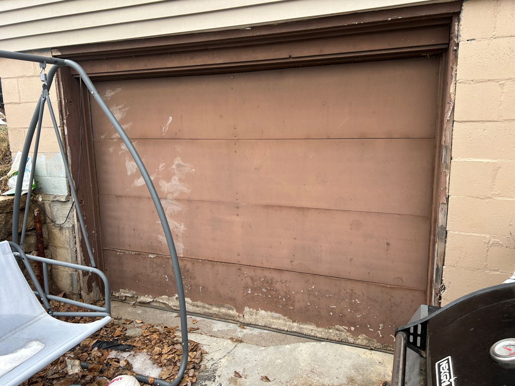 Garage door panel repair showing an aging steel garage door with rusted and deteriorated lower panels before replacement.