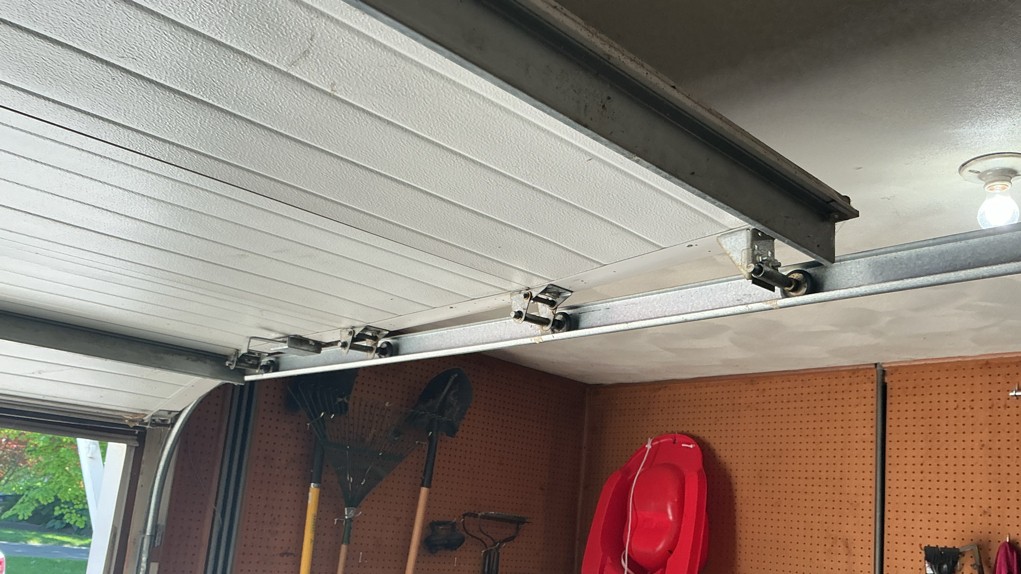 Garage door roller repair showing the overhead track, rollers, and hinge assembly on a residential garage door